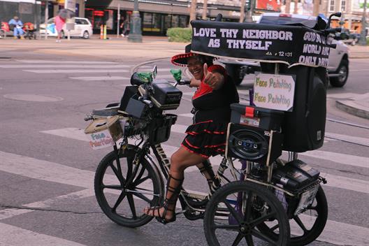 Christian Dinters Beitrag, aufgenommen in den USA, zeigt eine fröhlich winkende Frau auf einem Fahrrad, das mit einer Musikanalage ausgerüstet und mit Bibelzitaten geschmückt ist. 